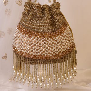 May include: A gold beaded drawstring bag with a white pearl beaded body and a gold beaded top. The bag has a fringe of dangling pearls and gold beads. The handles are also gold beaded.