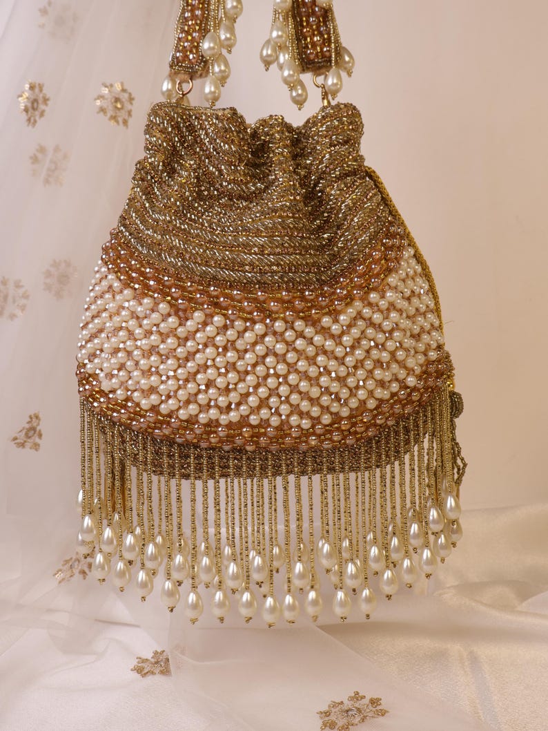 May include: A gold beaded drawstring bag with a white pearl beaded body and a gold beaded top. The bag has a fringe of dangling pearls and gold beads. The handles are also gold beaded.