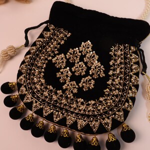 May include: A black velvet pouch with detailed gold embroidery and pearl bead embellishments. The pouch has a drawstring closure and is decorated with black velvet tassels with gold trim. A pearl beaded handle is also visible.