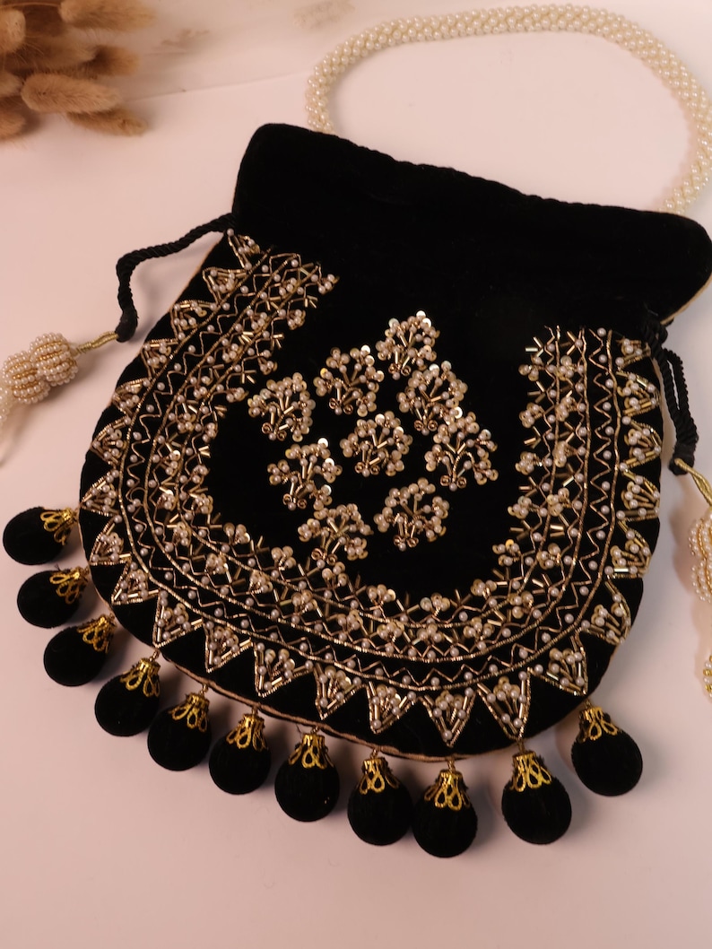 May include: A black velvet pouch with detailed gold embroidery and pearl bead embellishments. The pouch has a drawstring closure and is decorated with black velvet tassels with gold trim. A pearl beaded handle is also visible.