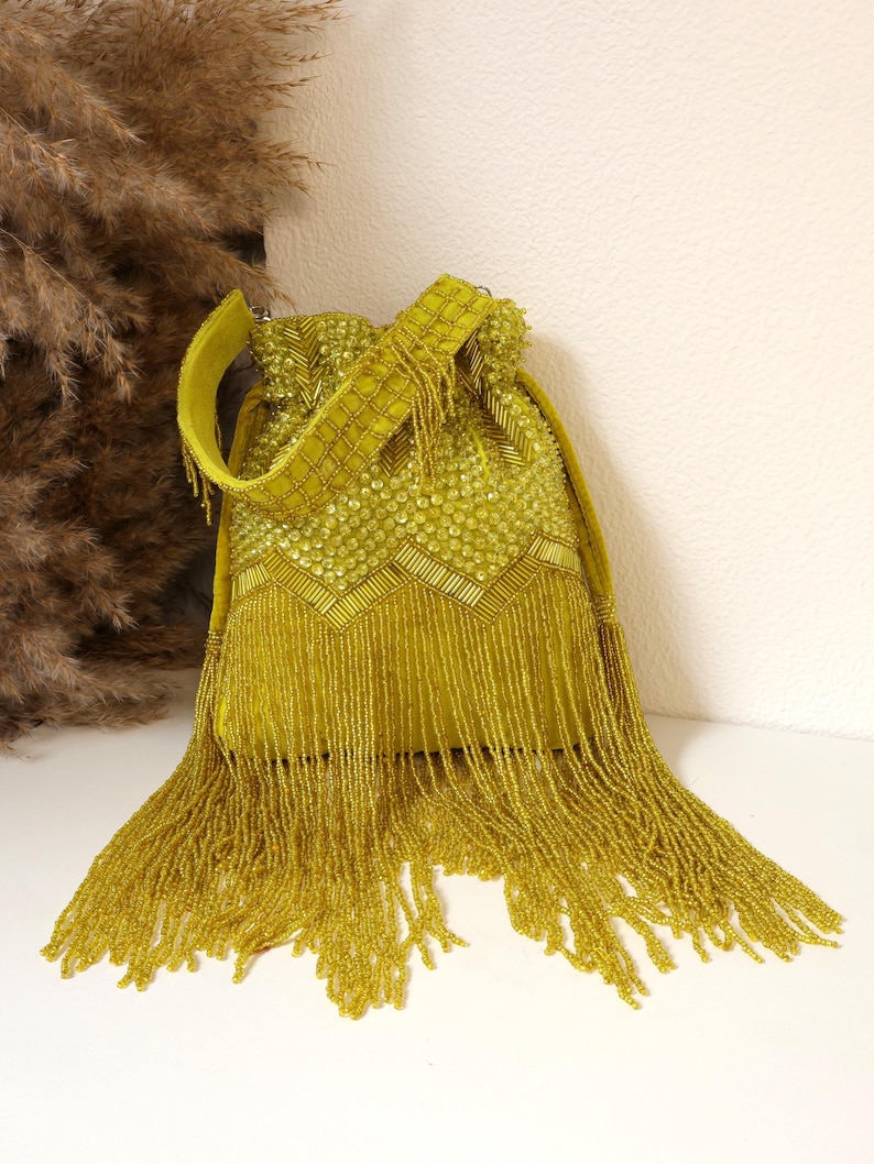 May include: A chartreuse drawstring handbag featuring an intricate exterior adorned with dense beadwork, including circular and linear patterns. The bag is finished with a long, flowing fringe of matching chartreuse beads that extends from the base.