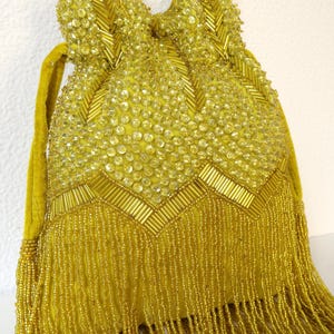 May include: A mustard yellow drawstring pouch bag featuring extensive beadwork and sequin embellishments. The exterior is decorated with a chevron pattern of cylindrical beads and circular sequins, finished with a long fringe of dangling yellow beads.