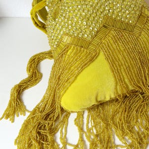 May include: A bright yellow velvet handbag featuring intricate beadwork and sequins in a chevron pattern. The bag is adorned with long, cascading yellow beaded fringe that hangs from the bottom, and it includes a matching yellow velvet handle.