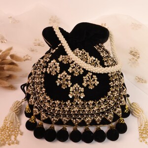 May include: A black velvet drawstring bag with gold embroidery and pearl detailing. The bag has a beaded pearl strap and tassels with black pom-poms. The design is ornate and elegant, suitable for special occasions.
