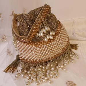 May include: A beaded drawstring bag in gold, bronze, and cream colors. The bag is covered in small beads and pearls, with a fringe of dangling pearls. The bag's opening is lined with a light tan fabric.