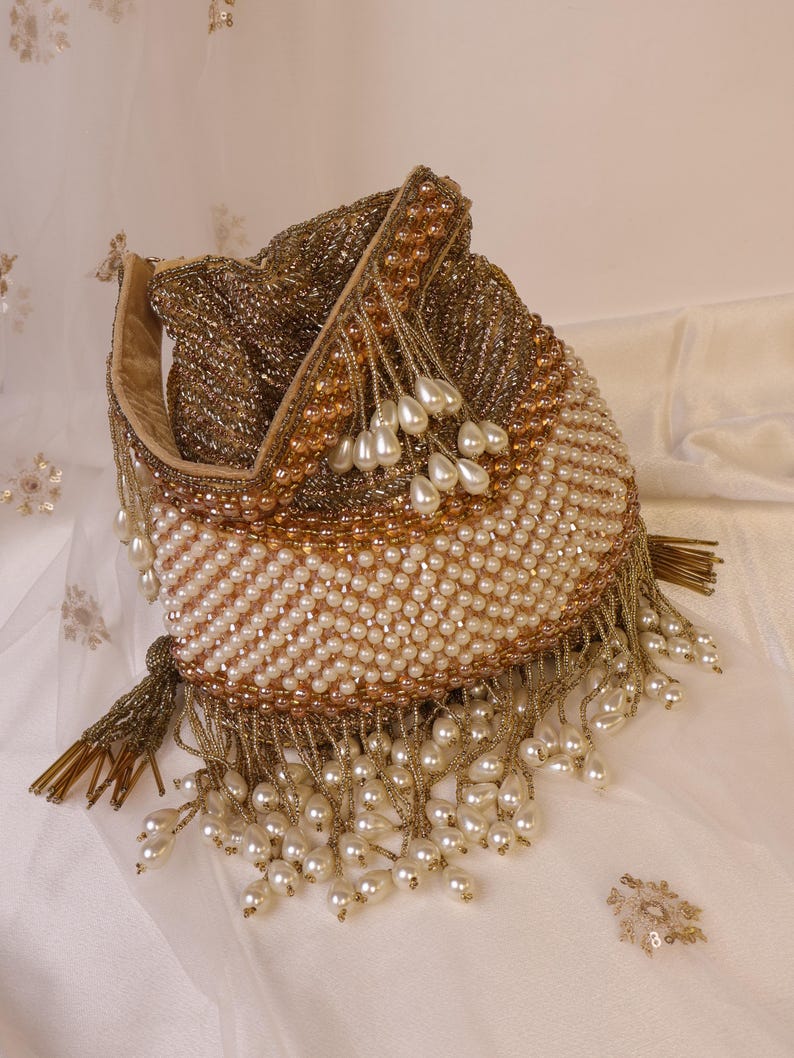 May include: A beaded drawstring bag in gold, bronze, and cream colors. The bag is covered in small beads and pearls, with a fringe of dangling pearls. The bag's opening is lined with a light tan fabric.
