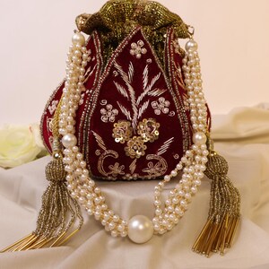 May include: A red velvet drawstring bag with gold and silver embroidery and embellishments. The bag has a long pearl and gold beaded strap with a large pearl accent.