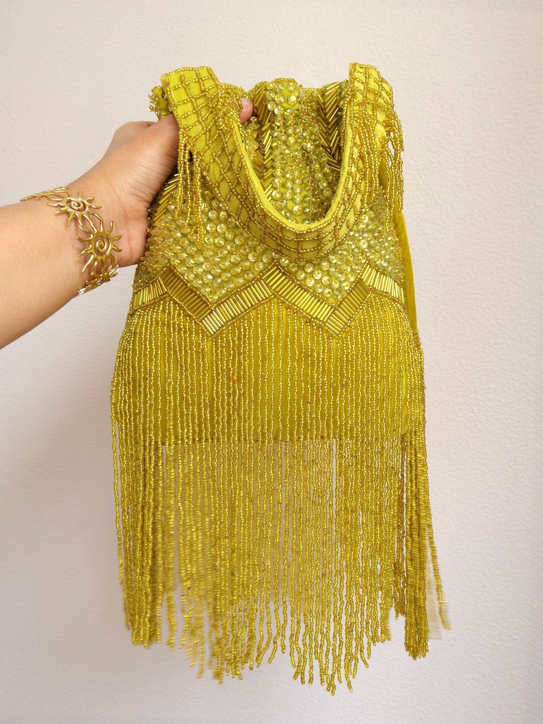 May include: A chartreuse handbag featuring intricate beadwork and sequins. The bag is adorned with a chevron pattern of tube beads and sequins on the upper section, while the lower portion consists of long, dangling beaded fringe strands.