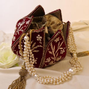 May include: A red velvet clutch purse with gold embroidery and pearl accents. The purse is shaped like a flower and has a beaded tassel.