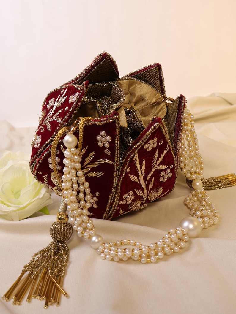 May include: A red velvet clutch purse with gold embroidery and pearl accents. The purse is shaped like a flower and has a beaded tassel.
