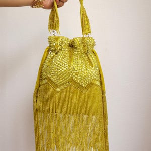 May include: A chartreuse drawstring handbag featuring an intricate exterior of sequins and glass beads arranged in a chevron pattern. The bag includes a single top handle and a long, dense fringe of matching chartreuse beads hanging from the base.
