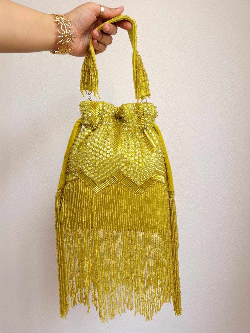 May include: A chartreuse drawstring handbag featuring an intricate exterior of sequins and glass beads arranged in a chevron pattern. The bag includes a single top handle and a long, dense fringe of matching chartreuse beads hanging from the base.