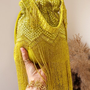 May include: A chartreuse drawstring handbag featuring extensive beadwork, including circular and tubular beads arranged in geometric patterns, and long, flowing beaded fringe that hangs from the lower section of the bag body.