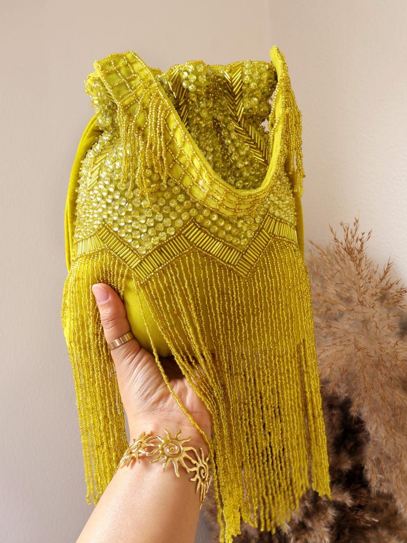 May include: A chartreuse drawstring handbag featuring extensive beadwork, including circular and tubular beads arranged in geometric patterns, and long, flowing beaded fringe that hangs from the lower section of the bag body.