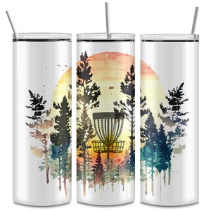 May include: A white, insulated tumbler with a lid and straw. The tumbler features a watercolor design of a disc golf basket in a forest with a sunset background. The design includes trees in shades of green, brown, and black.