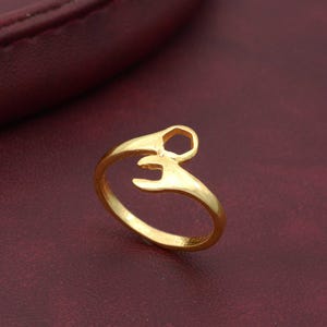 Puede incluir: Un anillo de oro con un diseño de dos manos sosteniendo una forma hexagonal.