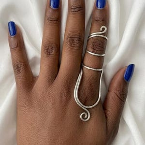 May include: A silver-colored ring with a unique design, featuring a curved shape that wraps around the finger. The ring has a swirl detail at the base and top. The nails are painted a vibrant blue.