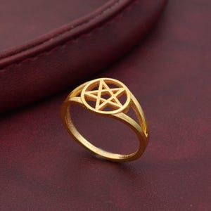 Può includere: Un anello dorato con un design a pentagramma. L'anello è in metallo e ha uno stile semplice ed elegante.