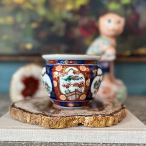 May include: A small, blue and red porcelain planter with gold accents and a floral design. The planter is sitting on a wooden slice with gold paint.