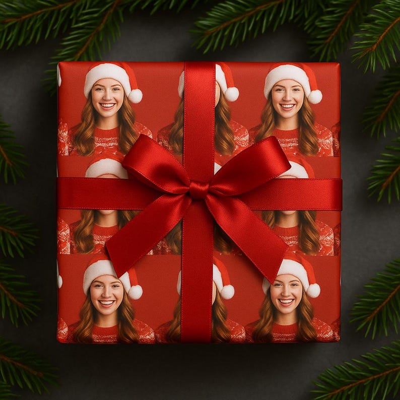May include: A wrapped gift with red wrapping paper featuring a repeating pattern of a smiling person wearing a Santa hat and a red sweater. A red satin ribbon and bow are tied around the gift. Green pine branches are in the background.