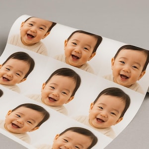 May include: A roll of stickers featuring multiple images of a smiling baby. The baby has dark hair and is wearing a light-colored sweater. The stickers are on a white background.