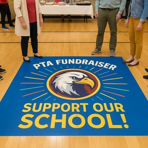 Op de afbeelding: Een blauwe vloermat met de tekst "PTA FUNDRAISER" en "SUPPORT OUR SCHOOL!" in het geel. De mat heeft een cirkelvormig embleem met een adelaarskop en een zonnestralenontwerp. Mensen staan rond de mat op een houten vloer.