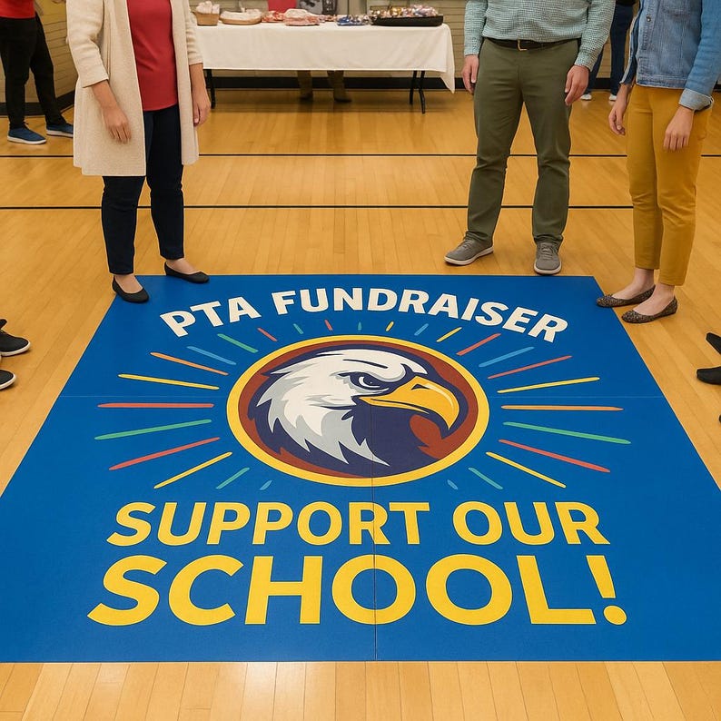 Op de afbeelding: Een blauwe vloermat met de tekst "PTA FUNDRAISER" en "SUPPORT OUR SCHOOL!" in het geel. De mat heeft een cirkelvormig embleem met een adelaarskop en een zonnestralenontwerp. Mensen staan rond de mat op een houten vloer.