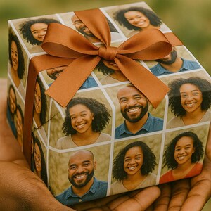 May include: A wrapped gift box featuring a collage of smiling faces, tied with a brown ribbon and bow. The wrapping paper displays a grid of individual portraits. The box is held in a person's hands.