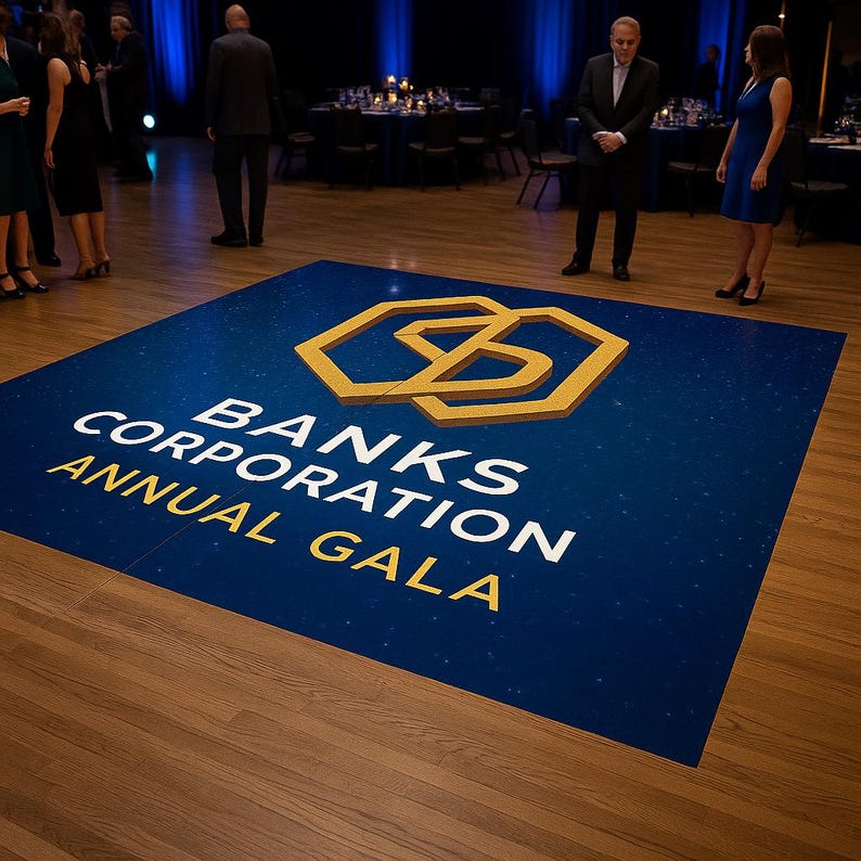 Op de afbeelding: Een blauwe dansvloer met een gouden geometrisch logo en de tekst "BANKS CORPORATION ANNUAL GALA". De vloer staat op een houten vloer in een grote evenementenruimte. Mensen staan rond de dansvloer.