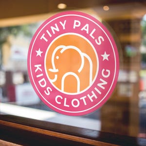 May include: A pink and white circular sticker with the text "Tiny Pals Kids Clothing" and a white outline of an elephant in an orange circle.