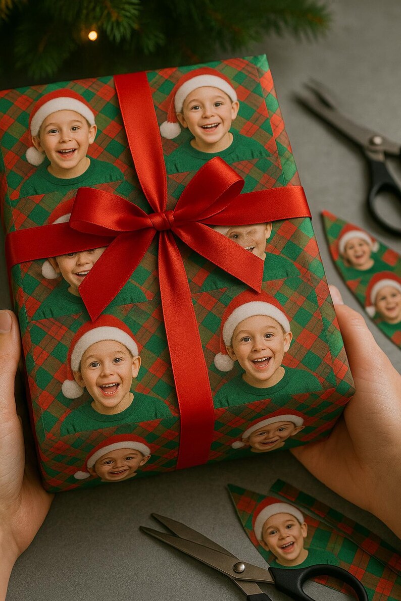 May include: A wrapped gift featuring a repeating pattern of a smiling child wearing a Santa hat and green shirt. The wrapping paper has a red and green plaid design. A large red ribbon is tied around the gift. Scissors are nearby.