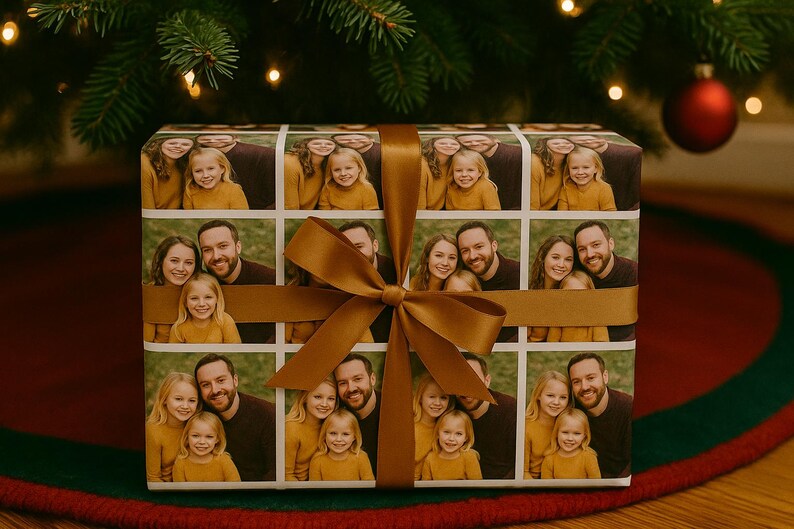 May include: A wrapped gift with a custom photo collage on the wrapping paper. The gift is tied with a wide, golden-brown ribbon and bow. The gift is under a Christmas tree with a red ornament.