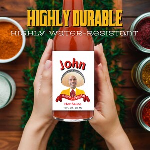 May include: A red hot sauce bottle with a white label. The label features a picture of a man wearing a sombrero and a yellow shirt. The label reads "John" and "Happy Birthday" with a red ribbon. The bottle states "Hot Sauce" and "10 FL. OZ. - 296 ML".