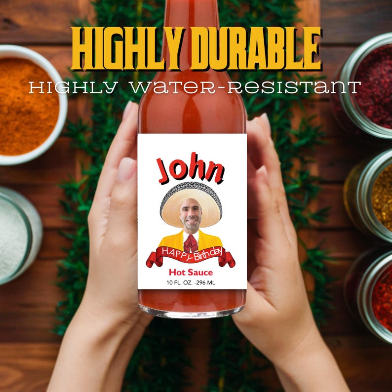May include: A red hot sauce bottle with a white label. The label features a picture of a man wearing a sombrero and a yellow shirt. The label reads "John" and "Happy Birthday" with a red ribbon. The bottle states "Hot Sauce" and "10 FL. OZ. - 296 ML".