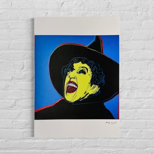 May include: A colorful pop art print of a woman wearing a black witch's hat and a yellow face with a wide open mouth. The background is blue. The print is signed "Andy Warhol".