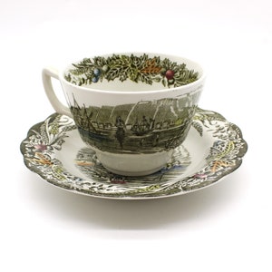 Puede incluir: Un juego de taza y platillo vintage con un patrón floral verde y marrón. La taza y el platillo presentan una escena de un puerto con barcos y edificios.