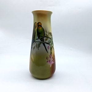 Könnte beinhalten: Eine grüne und weiße Keramikvase mit einem Blumendesign und zwei grün-gelben Vögeln, die auf einem Ast sitzen.