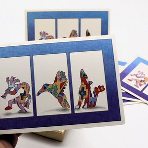 Op de afbeelding: Drie kleurrijke kaarten met een blauwe rand en een witte binnenkant. Elke kaart heeft een ander gestileerd dierontwerp in een geometrisch patroon. De dieren zijn een vogel, een hert en een vis.
