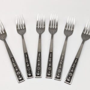 May include: Six silver forks with decorative handles. The handles feature a detailed pattern with circular and rectangular elements. The forks are arranged on a white surface, showcasing their design and craftsmanship. Suitable for a vintage dining setting.