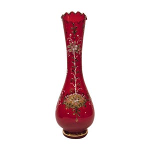 Puede incluir: Un jarrón de vidrio rojo con un borde dorado y diseños florales intrincados en blanco y dorado.
