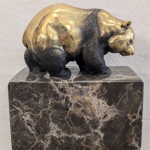 May include: A bronze bear sculpture with a gold-colored body and black accents, mounted on a dark marble base. The bear is depicted in a walking pose, showcasing detailed craftsmanship. This decorative piece is suitable for home decor.