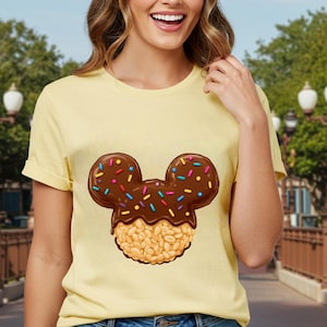 May include: A yellow t-shirt with a cartoon image of a Mickey Mouse-shaped rice krispie treat with chocolate and colorful sprinkles.