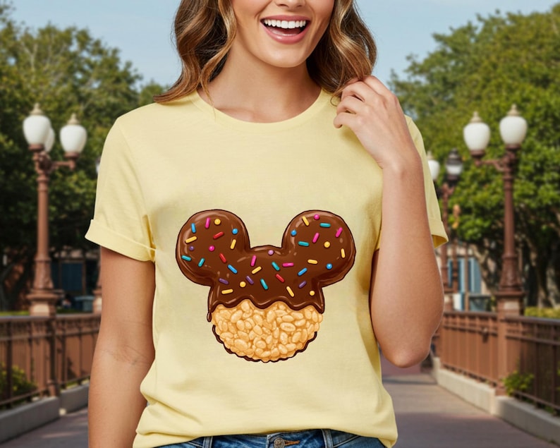 May include: A yellow t-shirt with a cartoon image of a Mickey Mouse-shaped rice krispie treat with chocolate and colorful sprinkles.