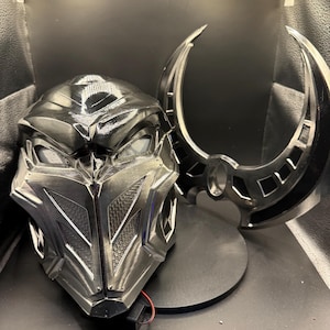 May include: A black and silver helmet with a detailed design and a matching black and silver weapon. The helmet has a visor and the weapon is a crescent-shaped blade.