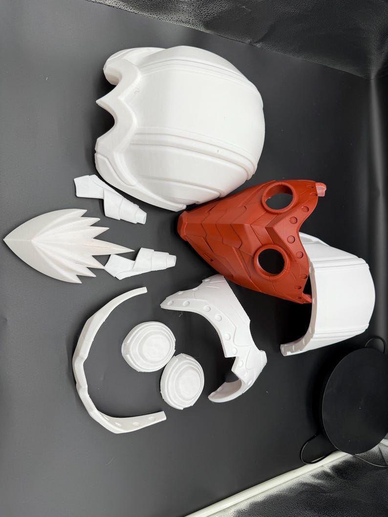May include: A set of white and red plastic helmet pieces for cosplay or costume making. The pieces include a helmet dome, a face mask, and several smaller pieces.