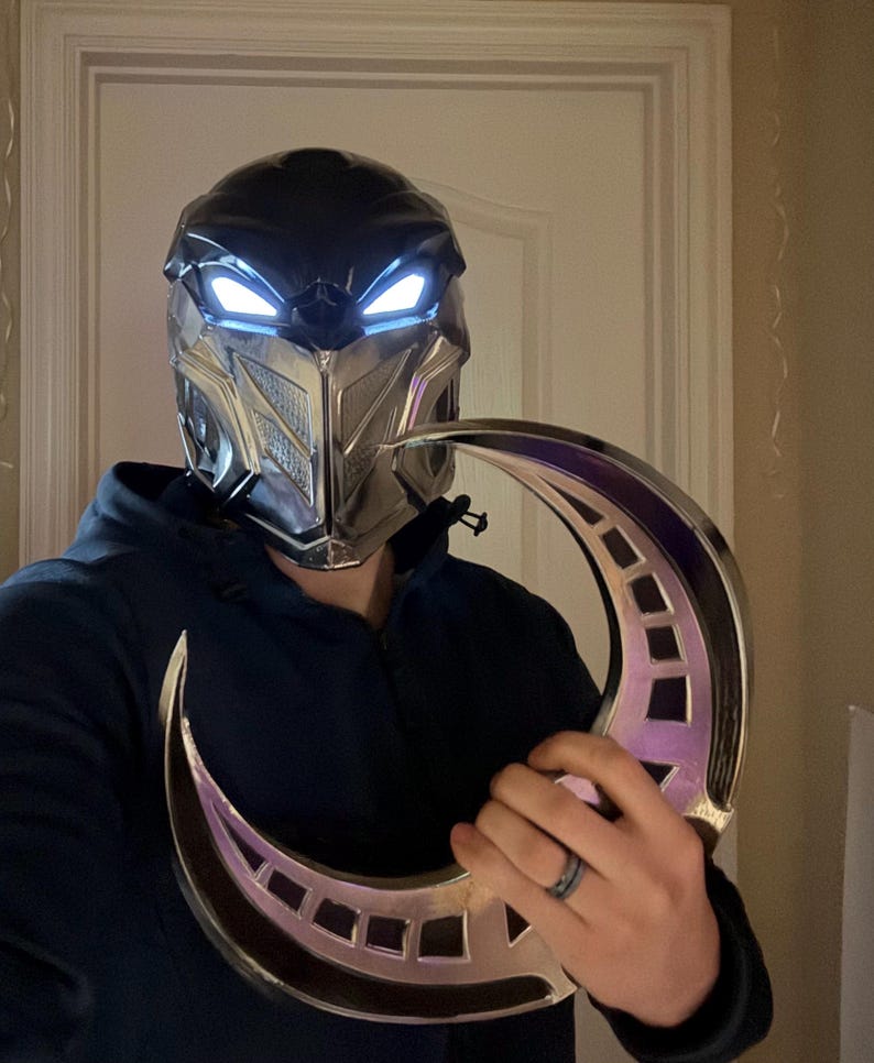 May include: A silver and black helmet with glowing blue eyes and a silver crescent moon prop.
