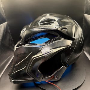May include: A black helmet with a blue light, a red wire, and a black battery pack.