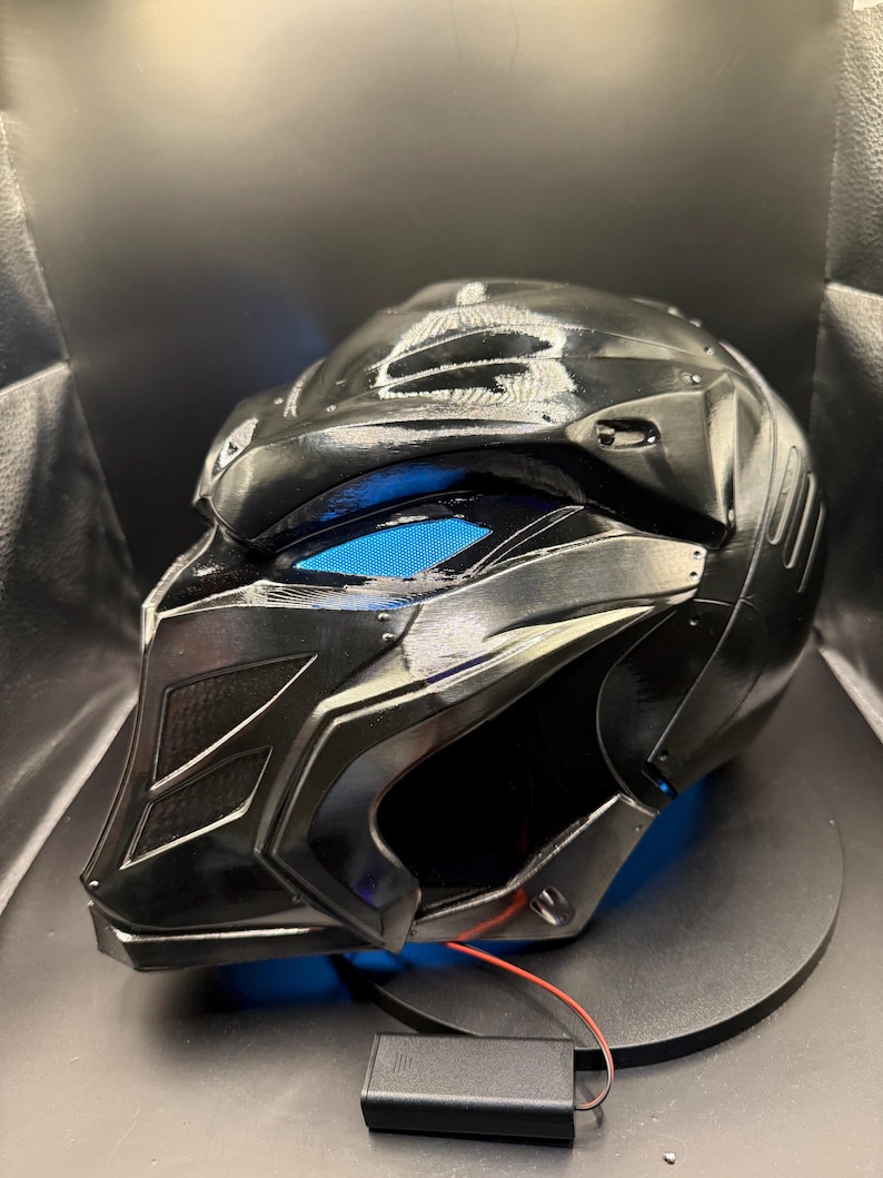May include: A black helmet with a blue light, a red wire, and a black battery pack.