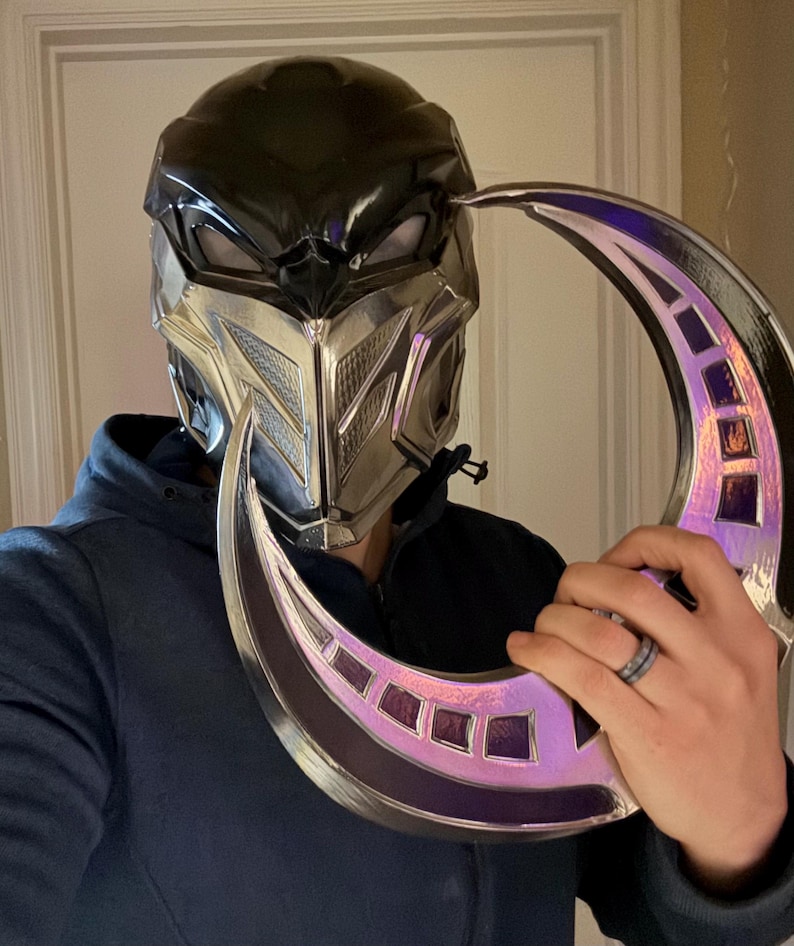 May include: A silver and black helmet with a crescent-shaped blade. The helmet has a black visor and a silver faceplate with a geometric design. The blade is silver with a purple iridescent finish.