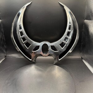 May include: A silver-colored metal crescent moon-shaped object with intricate details and a black center. The object is on a black circular base.